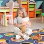 a girl sitting on the floor holding a stuffed animal
