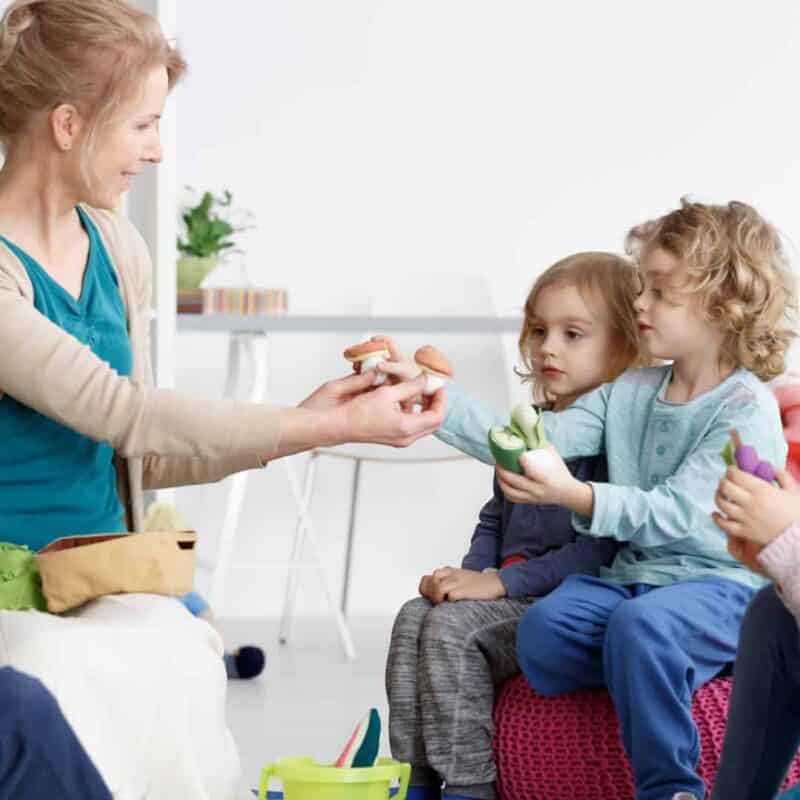 A woman giving a small mushroom to a group of children