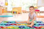 Child sitting on colorful alphabet rug.